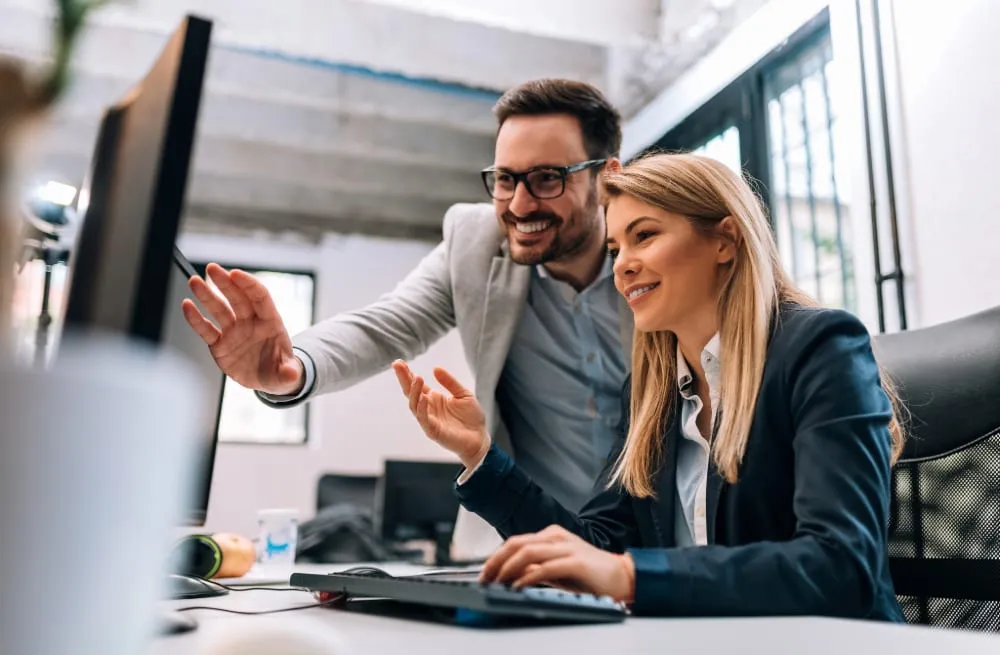 Dua anggota tim mendiskusikan sistem yang sedang berjalan di depan monitor
